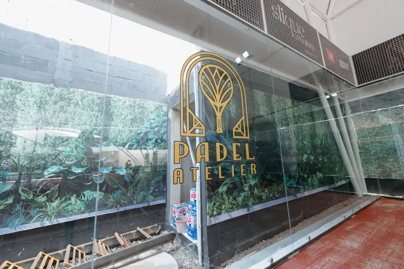 Gold Padel Atelier logo on the glass in front of the green wall