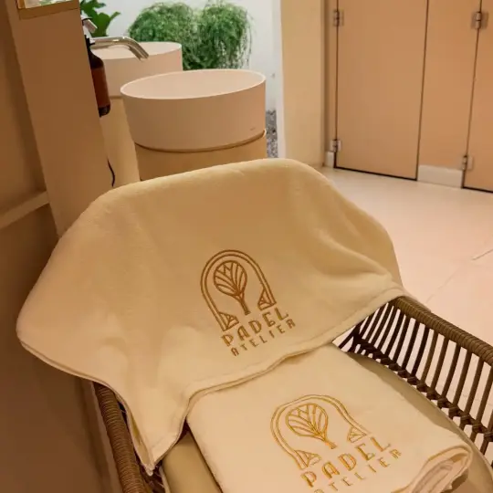 Cream towels embroidered with the gold Padel Atelier logo